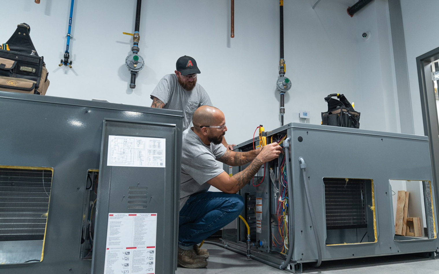 Two technicians working on HVAC units in a tech school work area.