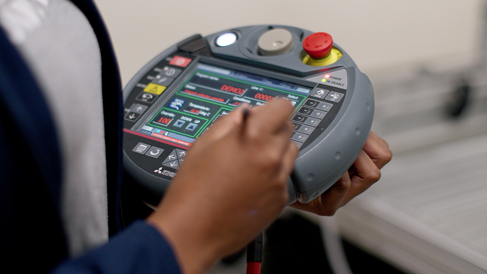 Kettering University student trains a robot using a robot teaching pendant from Mitsubishi Electric.